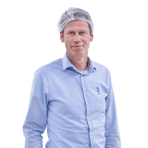 A person wearing a light blue button-up shirt and a white hairnet stands facing the camera. The shirt features a small logo on the left side. The person has a slight smile and appears against a plain background.