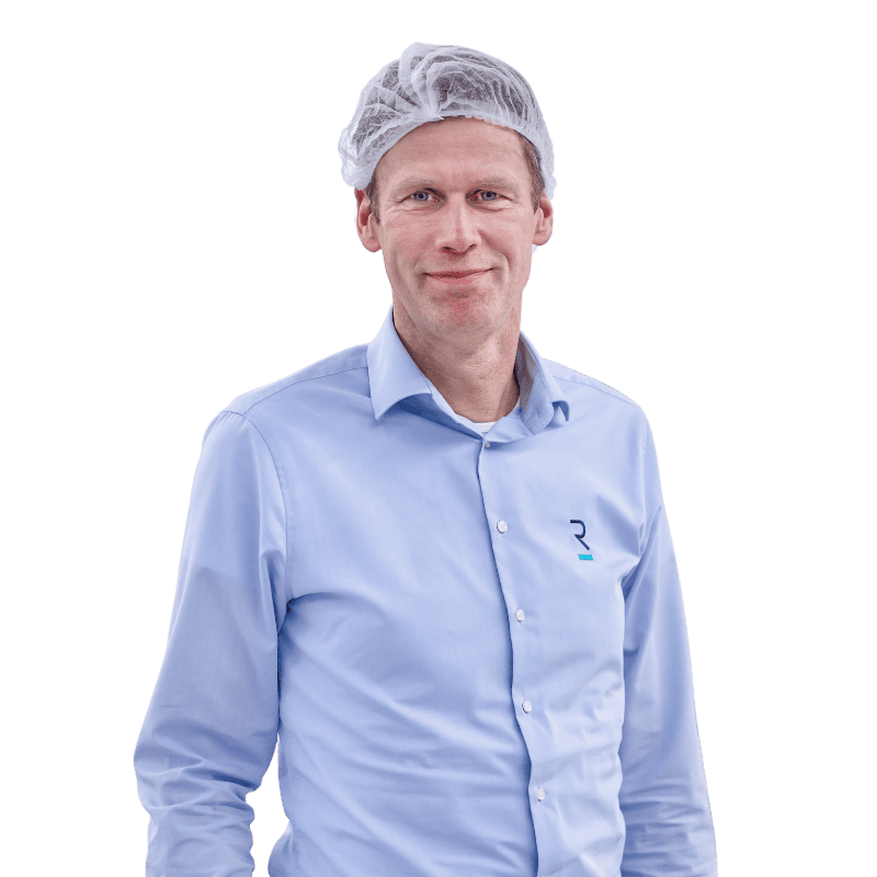 A person wearing a light blue button-up shirt and a white hairnet stands facing the camera. The shirt features a small logo on the left side. The person has a slight smile and appears against a plain background.