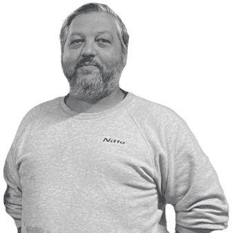 A grayscale image of a middle-aged man with a beard, wearing a light-colored sweatshirt with the word 