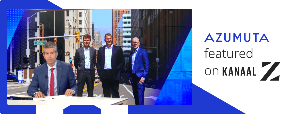 Image of the Kanaal Z submission with the presenter before a screen where three employees of Azumuta are displayed. They're standing in the streets of Detroit, smiling for the camera.
