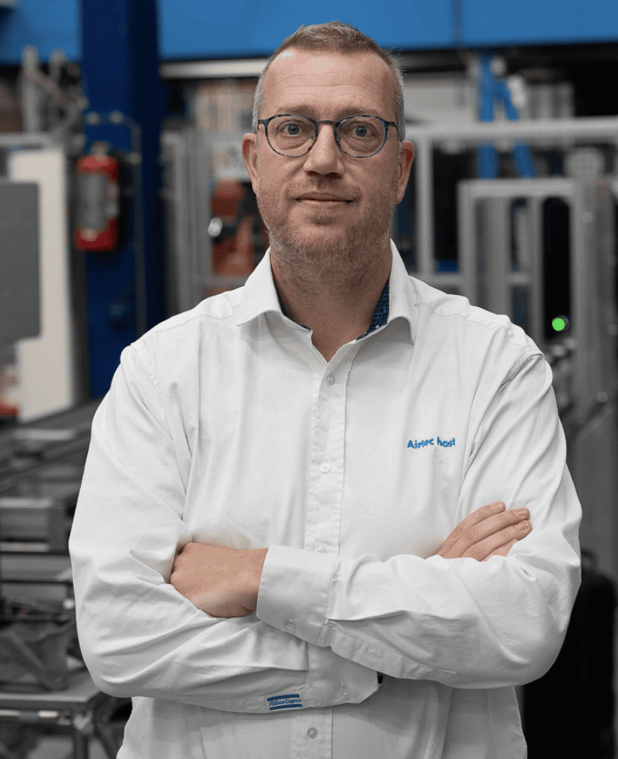 Profile picture of Johan Dom, VP of Process Engineering at Atlas Copco, posing for the camera. He's wearing a white button shirt with the Atlas Copco logo and glasses. His arms are crossed.