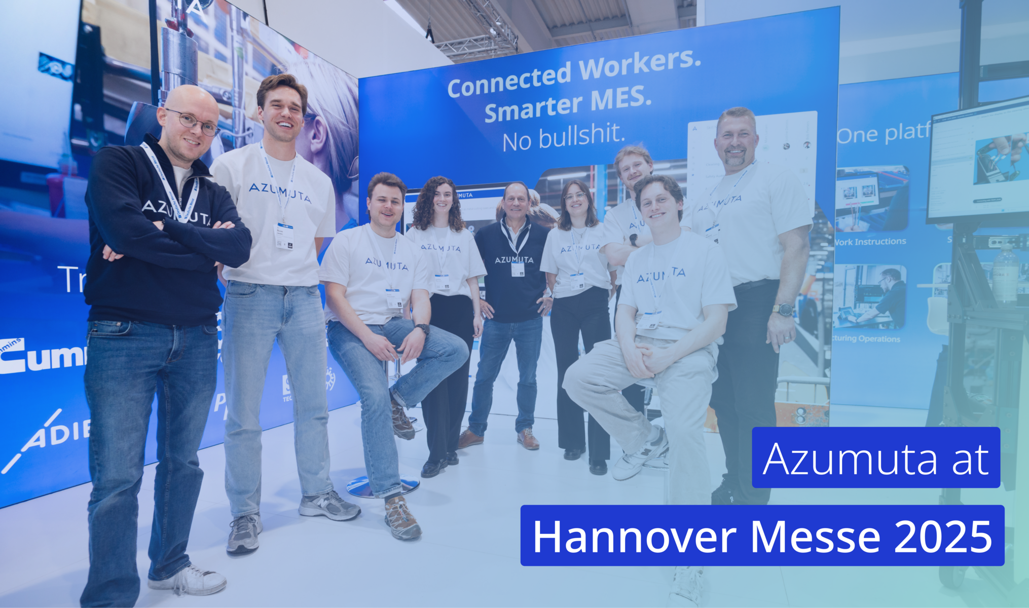 Azumuta team at their Hannover Messe 2025 booth, standing in front of a blue display with the slogan “Connected Workers. Smarter MES. No bullshit.” Visible demo setup and branding elements in the background.